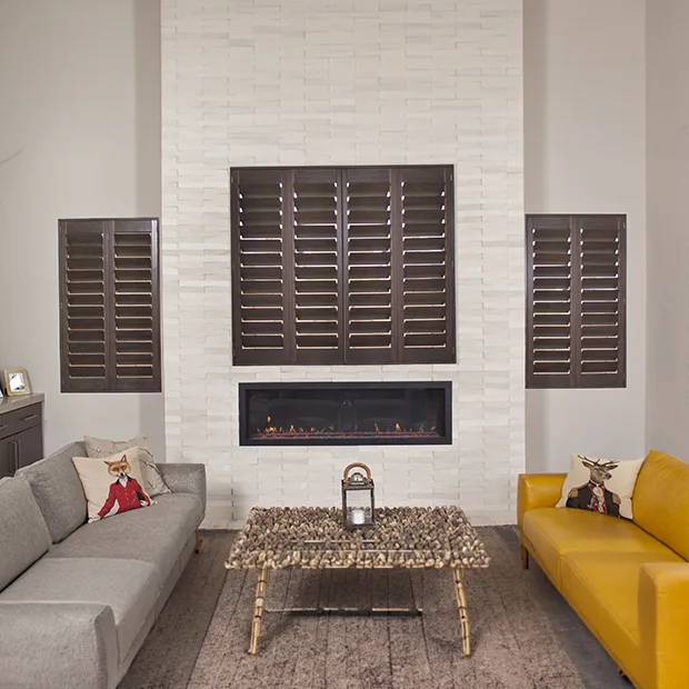 Dark wood interior shutters on windows in a white living room with a fireplace