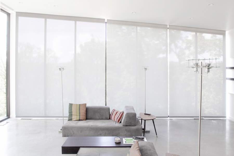 Motorized window shades make controlling natural light effortless in your Miami great room. White motorized shades on a wall of tall great room windows
