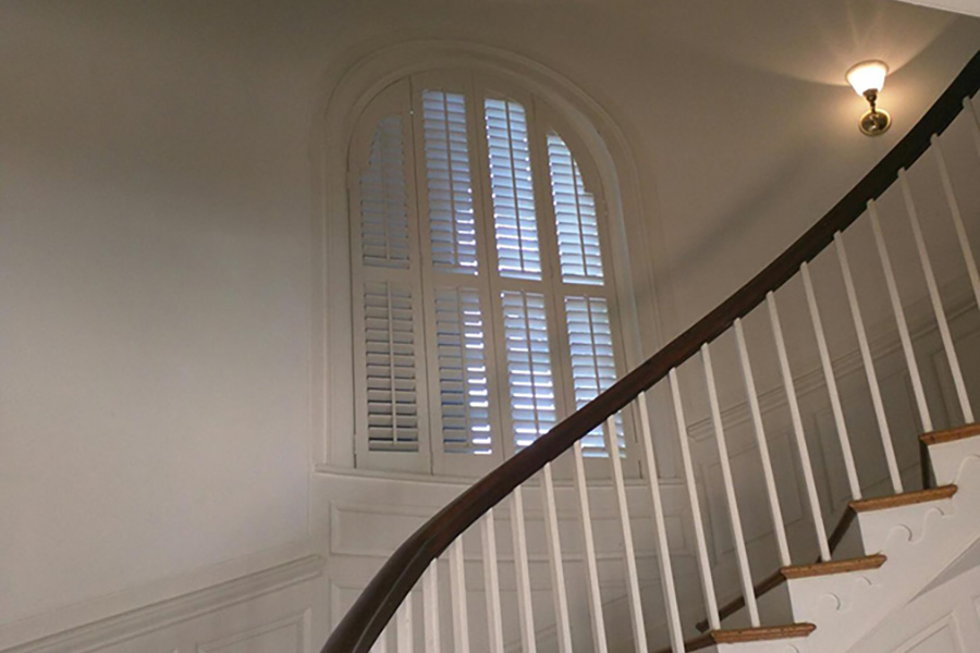 White Polywood shutters on an arched window in a stairwell