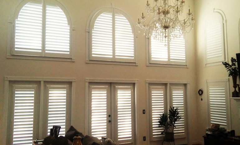 Family room in open concept Miami home with plantation shutters on tall windows.