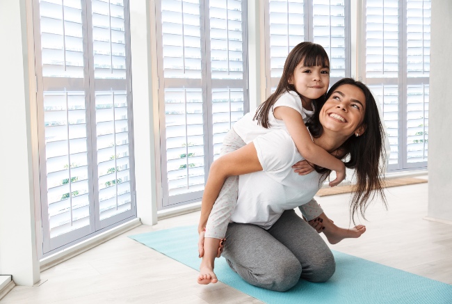 Mom and girl on yoga mat in room with plantation shutters