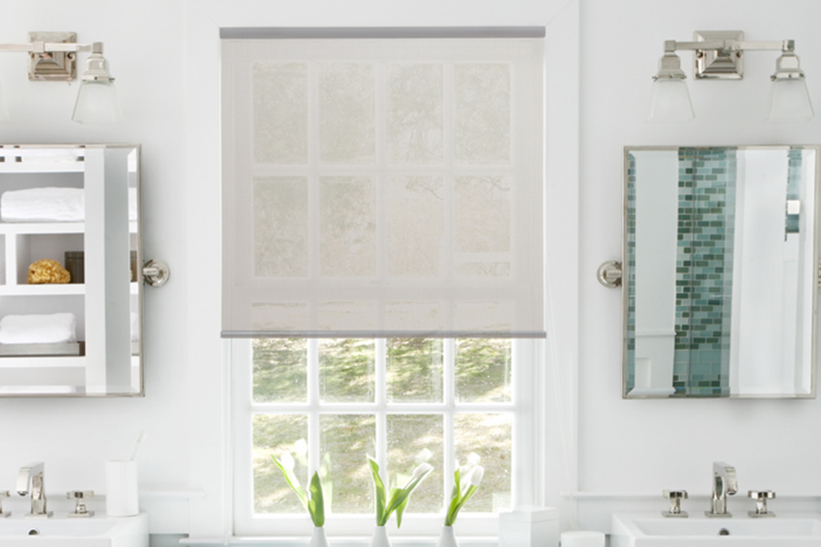 Light gray roller shade on a single window in a white bathroom.