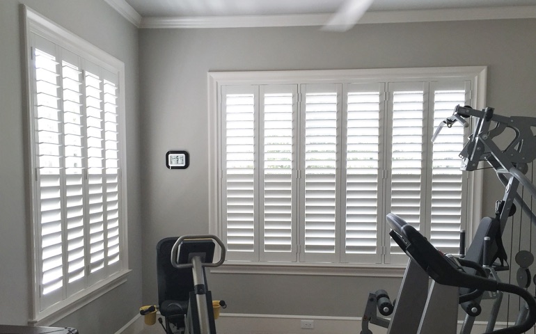 Draft-blocking window treatments are vital in rooms with windows on more than one wall. Miami exercise room with shuttered windows.