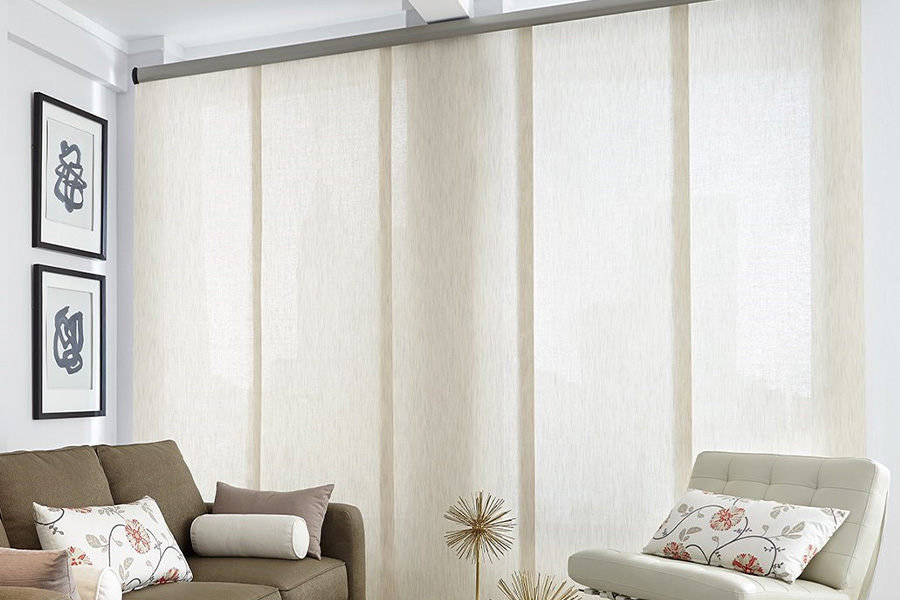 Find window treatments to complete any interior design among our extensive selection at Sunburst Shutters Miami.  Long off-white window shades on a tall window in a modern living room